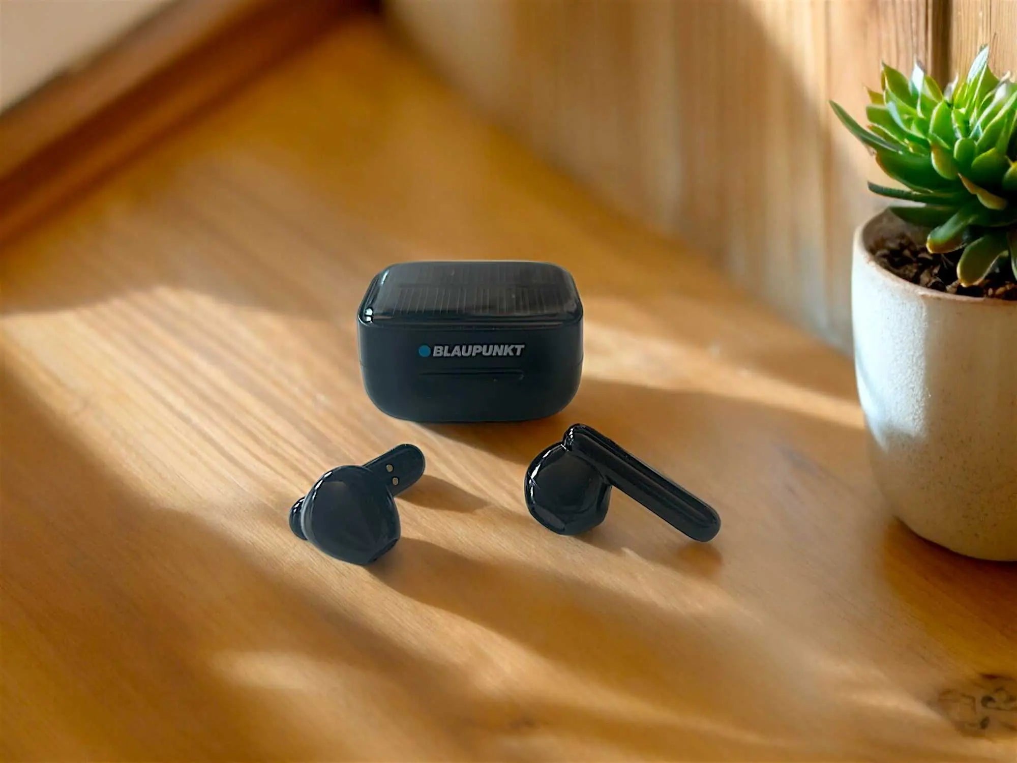Schwarze TWS 40-Kopfhörer mit geschlossenem Ladecase leicht von oben auf Holzuntergrund aufgenommen.